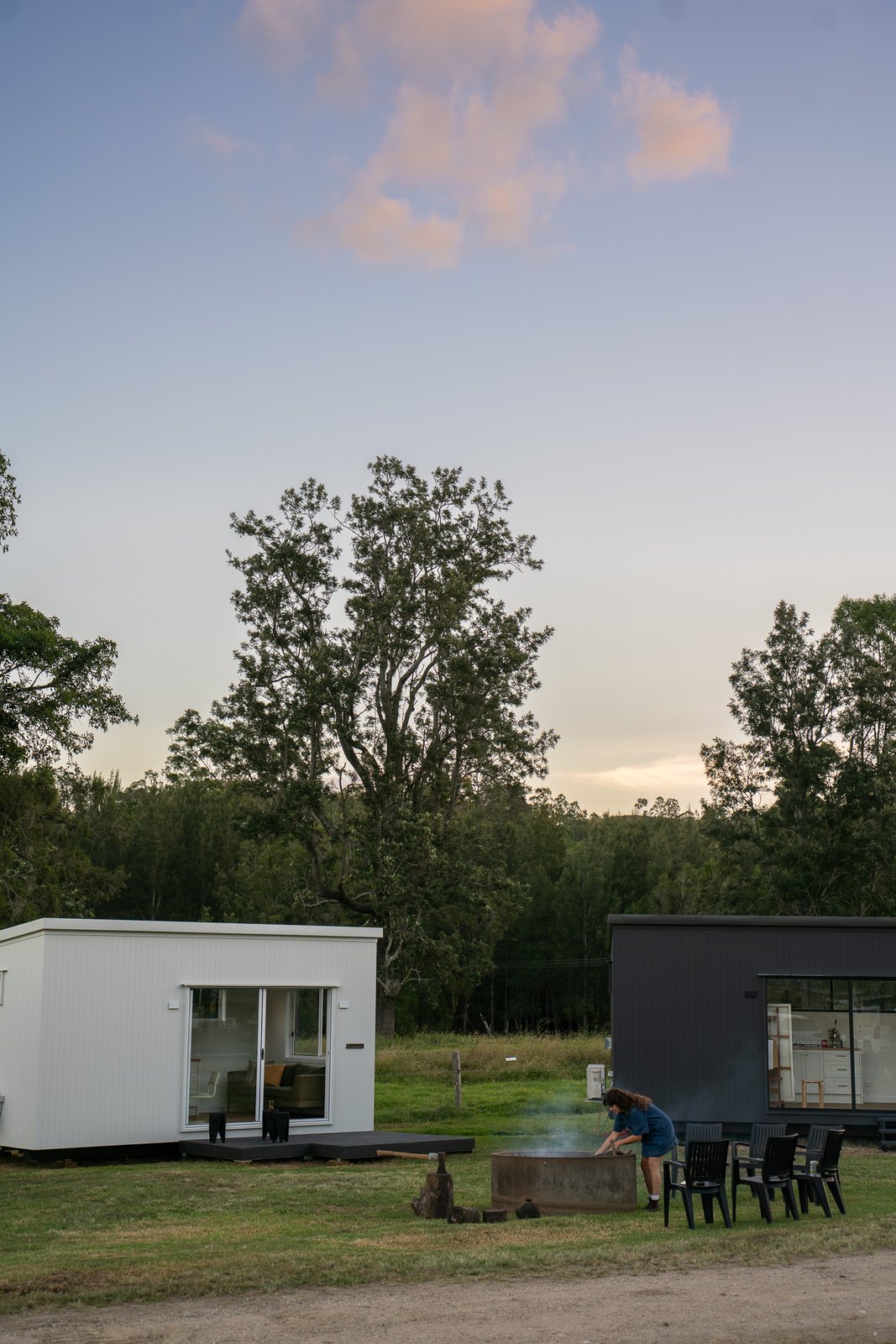 A white and a dark second home side by side on a paddock at dusk, chairs set around a fire pit